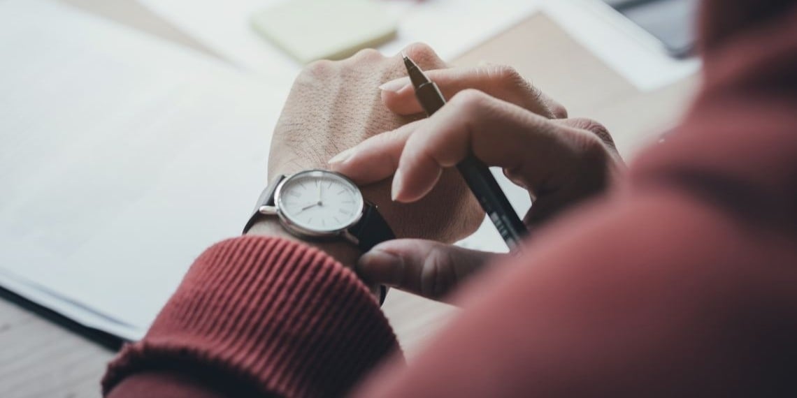 Nonprofit fundraiser managing his time and checking his watch while writing a donor letter.