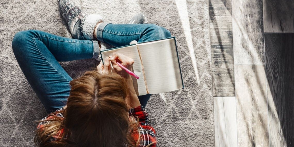 Woman sitting on the ground in cozy socks, writing in a notebook during the holiday season