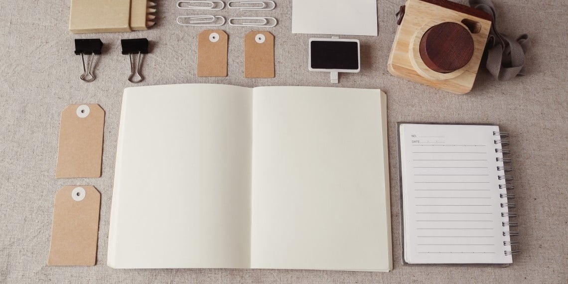 Open blank notebook flat on a table next to paper clips, labels, a smaller lined notebook