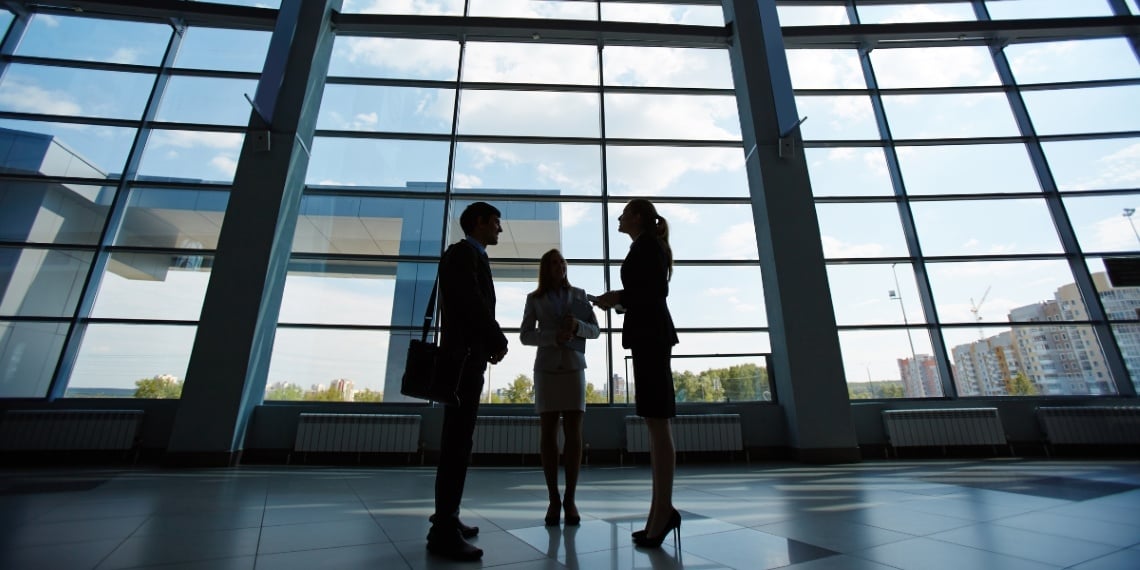 Three consultants discussing fundraising strategies while standing in front of a tall window