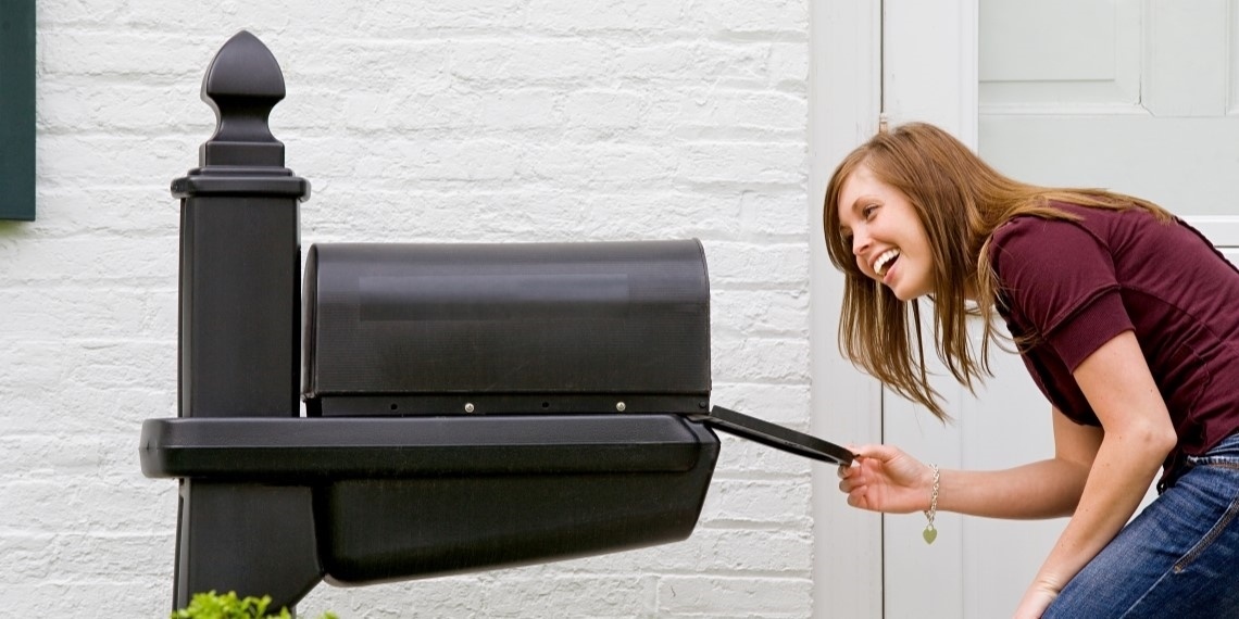 Woman smiling and looking into her mailbox, hoping for direct mail from a nonprofit for fundraising purposes