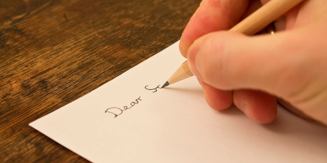 Close up of a nonprofit fundraising employee starting to write a donor letter with a pencil and white paper